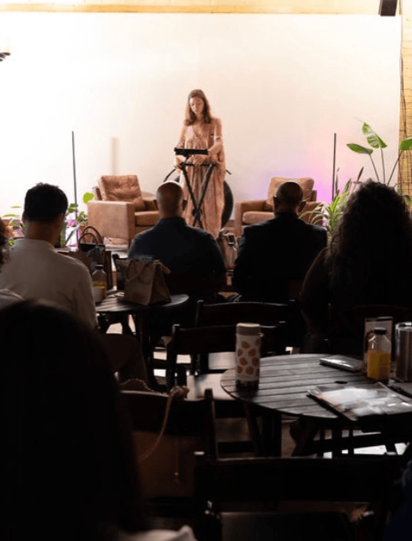 An audience seated at tables watching Margo Free perform on a small stage